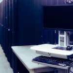Computador de tela preta diante de fileiras de racks de servidores em um data center