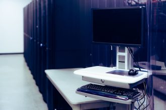 Computador de tela preta diante de fileiras de racks de servidores em um data center