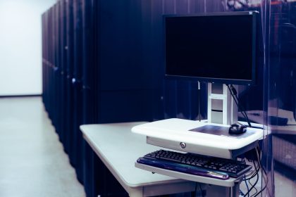 Computador de tela preta diante de fileiras de racks de servidores em um data center