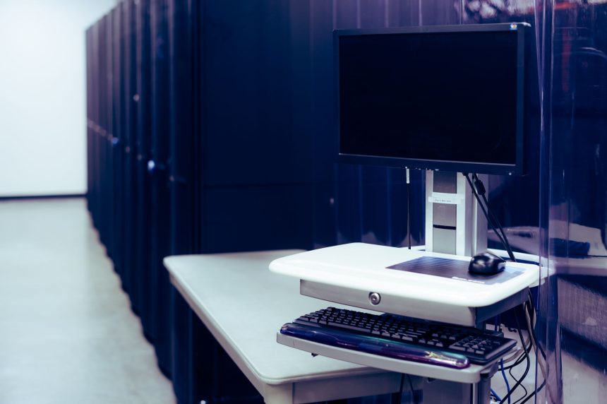 Computador de tela preta diante de fileiras de racks de servidores em um data center