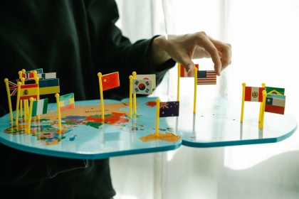 Mão organizando bandeiras de diferentes países sobre um mapa-múndi.