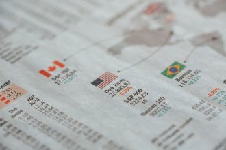Close de um jornal com estatísticas de mercados financeiros globais e bandeiras de diferentes países.