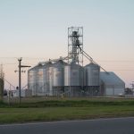 Silos metálicos de grãos ao lado de uma estrada rural em Córdoba, Argentina, ao entardecer.