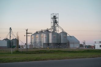 Silos metálicos de grãos ao lado de uma estrada rural em Córdoba, Argentina, ao entardecer.