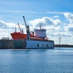 Navio-tanque atracado em um porto industrial, próximo a guindastes e instalações de armazenamento.
