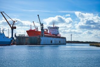 Navio-tanque atracado em um porto industrial, próximo a guindastes e instalações de armazenamento.
