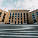 Exterior do Federal Reserve em Washington, visto de baixo, com bandeiras dos Estados Unidos e uma escadaria.