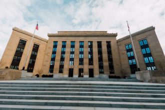 Exterior do Federal Reserve em Washington, visto de baixo, com bandeiras dos Estados Unidos e uma escadaria.