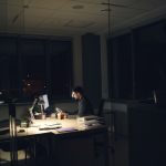 Homem trabalhando sozinho à noite em um escritório, iluminado pela luz da mesa.