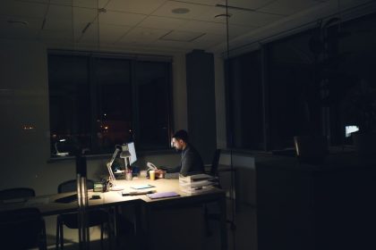 Homem trabalhando sozinho à noite em um escritório, iluminado pela luz da mesa.