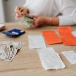 Pessoa usando uma calculadora e contando cédulas para planejar o orçamento doméstico.