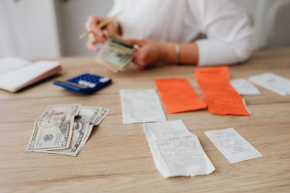 Pessoa usando uma calculadora e contando cédulas para planejar o orçamento doméstico.