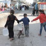 Crianças carregam recipientes de água por uma rua de Gaza.