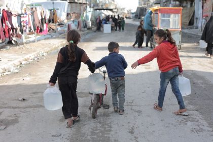 Crianças carregam recipientes de água por uma rua de Gaza.